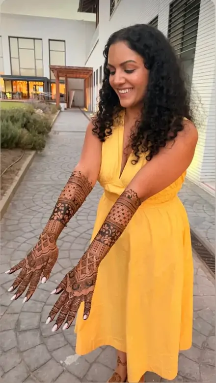 Bride in a yellow outfit with mehndi on both arms